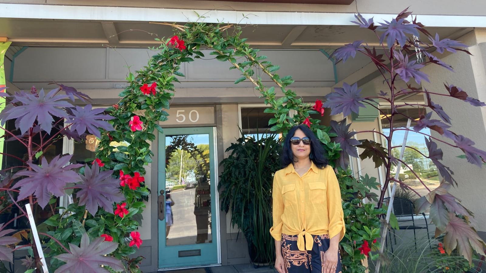 A woman poses in front of a colorful flower arch, embodying beauty and serenity at Kaya by Reema Salon.