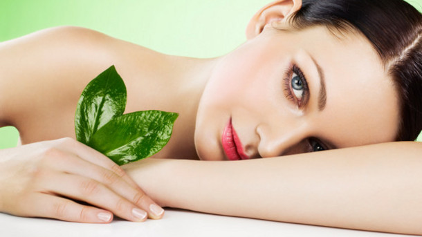 A beautiful woman holds a green leaf, showcasing the natural essence of Kaya by Reema Salon's facial services.