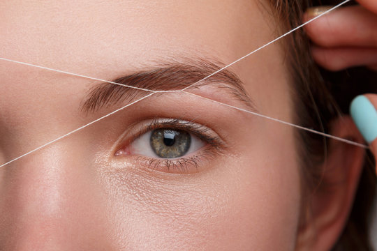 A woman skillfully uses thread to shape her eyebrows at Kaya by Reema Salon, showcasing expert facial services.