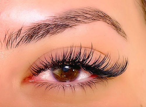 A detailed view of a woman's eye with extended eyelashes, reflecting grace and allure in a calming atmosphere.